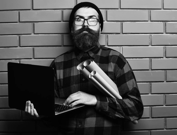 Bearded brutal caucasian hipster holding laptop and craft paper - Фото, изображение