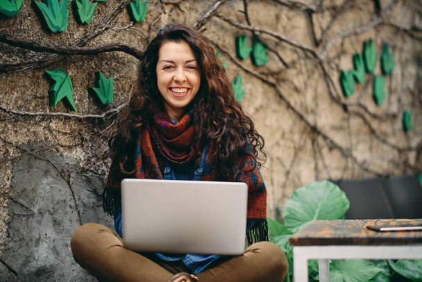 Mulher usando laptop e sorrindo enquanto está sentado no jardim
. - Foto, Imagem