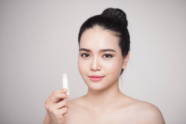Aziatische vrouw toepassing van hygiënische lippenbalsem over grijze achtergrond - Foto, afbeelding