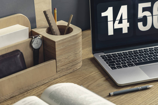 Close-up of wooden desk organizer with pencil and watch, computer, pen and book lying on the desk - Foto, afbeelding