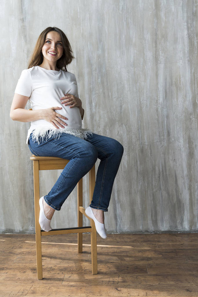 Pregnant girl on grey background in white t-shirt. - Foto, Imagem