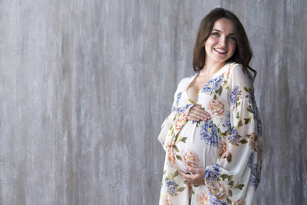 Έγκυος κορίτσι με φόρεμα σε φόντο γκρίζο τοίχο στο Studio. - Φωτογραφία, εικόνα