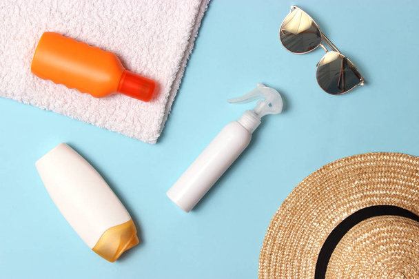 Sonnencreme, Handtuch, Hut, Brille auf farbigem Hintergrund. Kosmetik zur Vermeidung von Sonnenbrand. Draufsicht, Flatlay  - Foto, Bild
