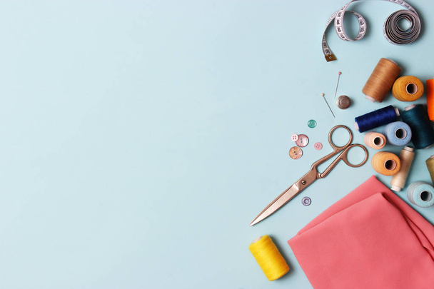 Sewing accessories and fabric on a blue background. Sewing threads, needles, pins, fabric, buttons and sewing centimeter. top view, flatlay - Φωτογραφία, εικόνα