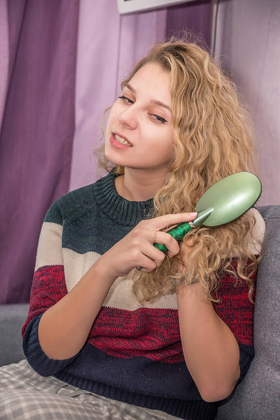 girl with Golden curly hair combs her hair and does her hair - Foto, Bild