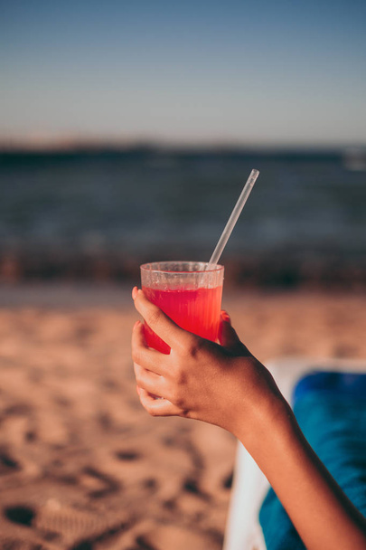 Girl holding red mai tai cocktail with a straw on the beach - Zdjęcie, obraz
