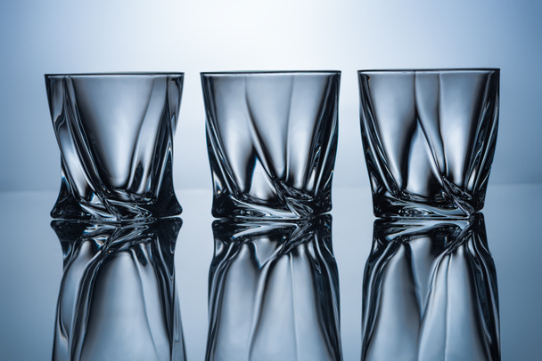 rij van drie lege whisky bril op grijs met reflecties - Foto, afbeelding