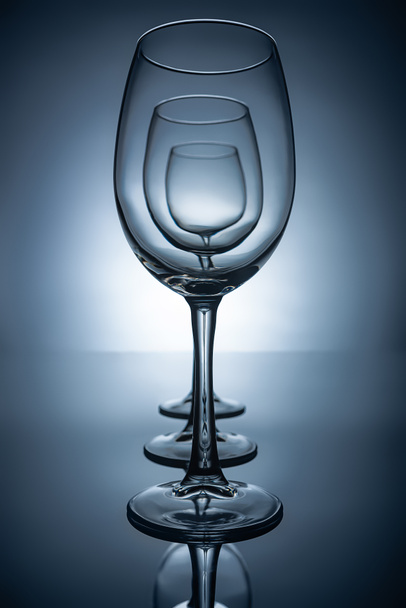 row of empty wine glasses with reflections, on grey - Foto, Bild