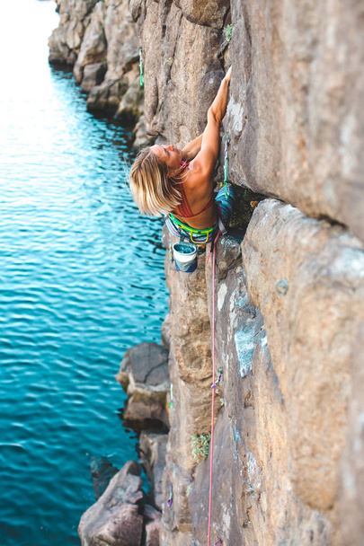 A hegymászó a víz felett. Egy nő mászik a rock. Képzési természetes terepen. Extrém sport. Hegymászó útvonal a tengerparton. - Fotó, kép