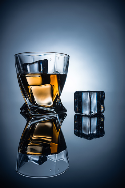 glass with cognac and ice cubes with reflections, on dark grey background - Photo, image