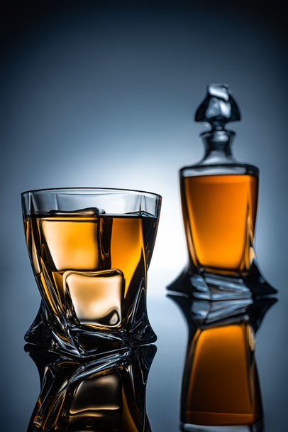 selective focus of whiskey glass with ice cubes and bottle, on grey - Zdjęcie, obraz