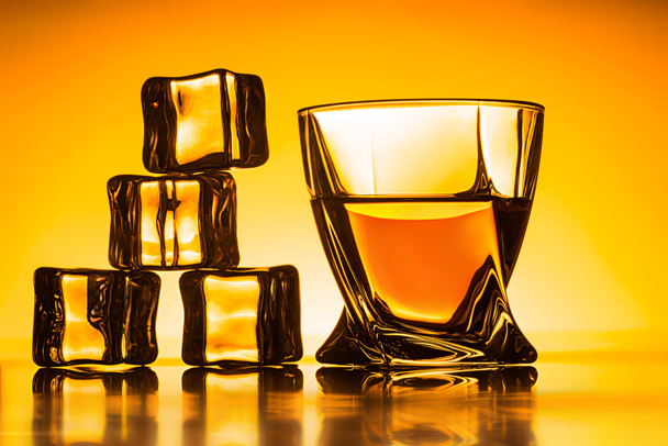 glass with whiskey and ice cubes near on orange background - Foto, Imagem