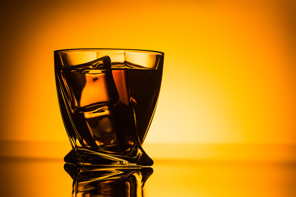 silhouette of glass with cognac and ice cubes on orange background - Photo, image