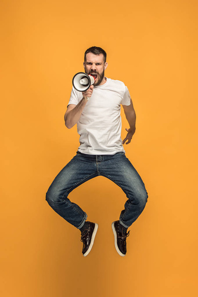 Jumping fan on orange background. The young man as soccer football fan with megaphone - 写真・画像