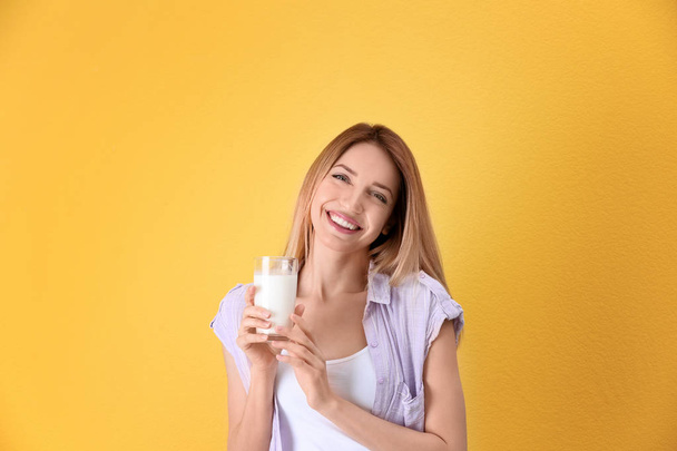 Beautiful young woman drinking milk on color background - Фото, изображение