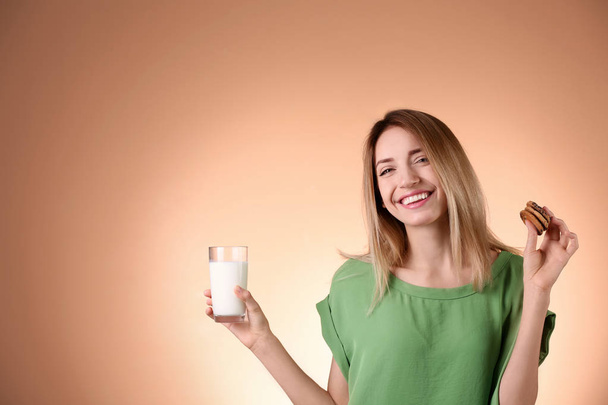 Beautiful young woman drinking milk with cookies on color background - Valokuva, kuva