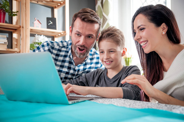 Onnellinen perhe käyttää kannettavaa tietokonetta yhdessä kotona
 - Valokuva, kuva