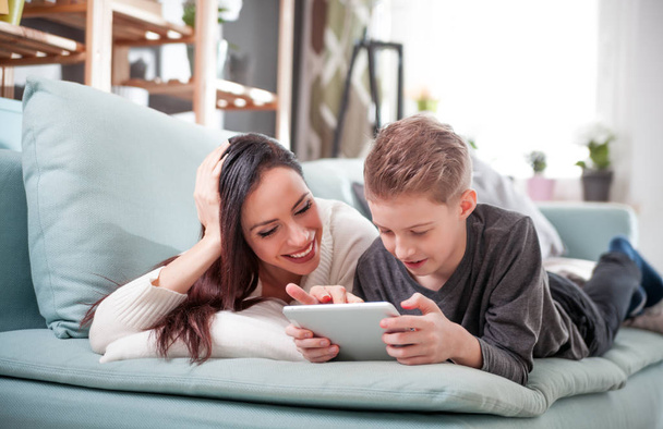 Äiti ja poika makaavat sohvalla ja käyttävät digitaalista tablettia kotona
 - Valokuva, kuva