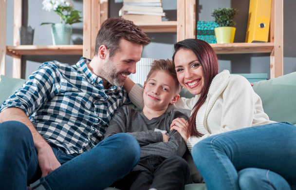 Молодая счастливая любящая семья, сидящая дома на диване
 - Фото, изображение