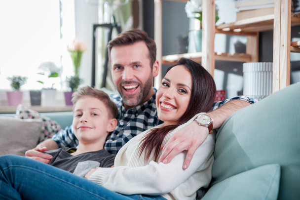 Молодая счастливая любящая семья, сидящая дома на диване
 - Фото, изображение