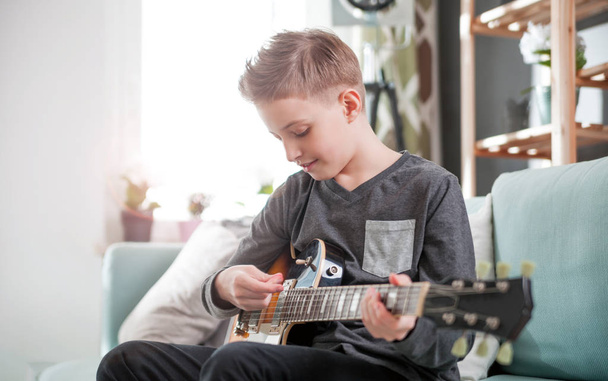 Young boy playing electric guitar on sofa at home - Фото, изображение