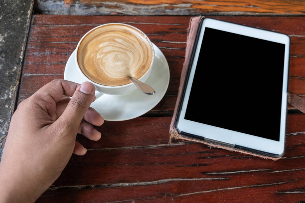 Café capuchino o latte en una taza blanca con espuma en forma de corazón sobre fondo de mesa de madera y un smatphone cerca
 - Foto, imagen