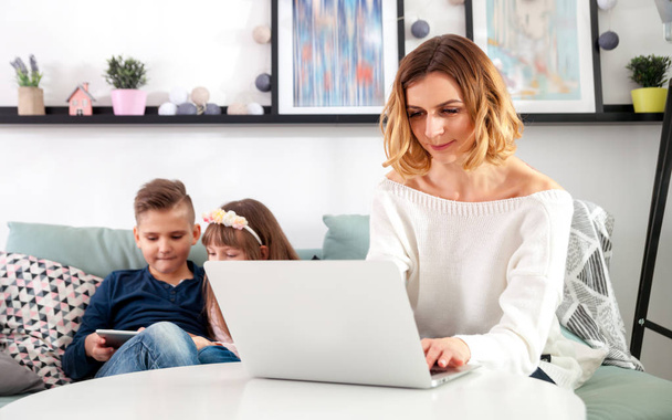 Young mother using laptop and children playing with tablet computer - Photo, image