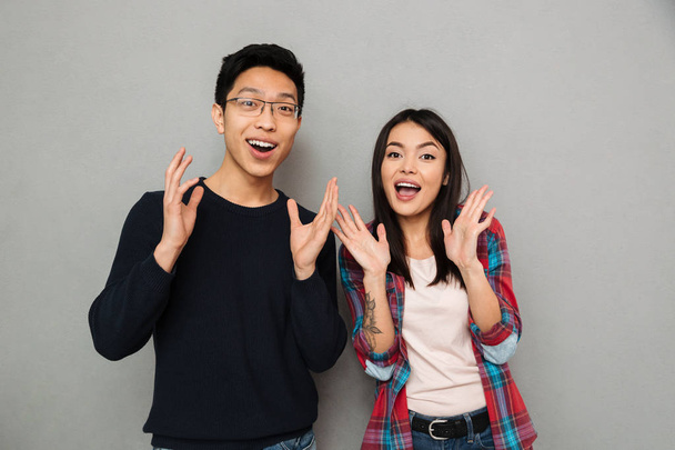 Image of excited young asian loving couple standing isolated over grey wall background looking camera. - Valokuva, kuva