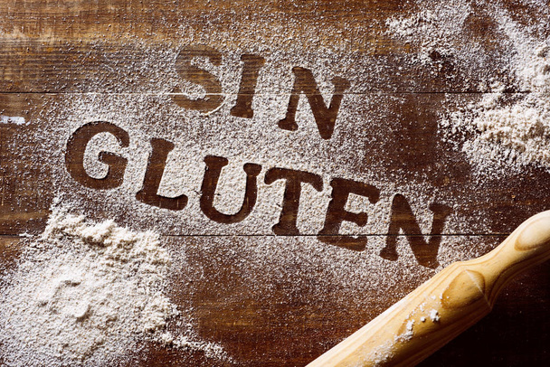 plan grand angle d'une table en bois saupoudré d'une farine sans gluten où vous pouvez lire le texte sin gluten, sans gluten écrit en espagnol, à côté d'un rouleau à pâtisserie
 - Photo, image