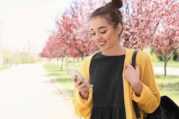 Young woman using phone outdoors on sunny day - Foto, imagen
