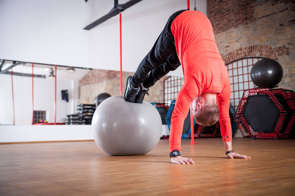 Sporty man working out with exercise ball at fitness gym - Fotó, kép
