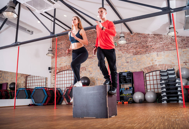 Sporty young couple doing squats on box at fitness gym - Foto, immagini