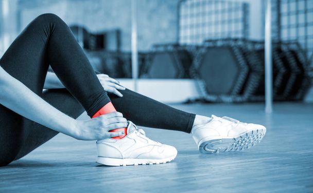Injured fit woman feeling pain in ankle at fitness gym - Fotó, kép