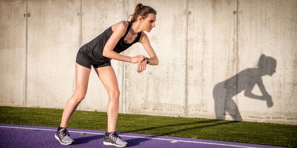 Woman running on stadium track and setting up fitness smart watch - Foto, Bild