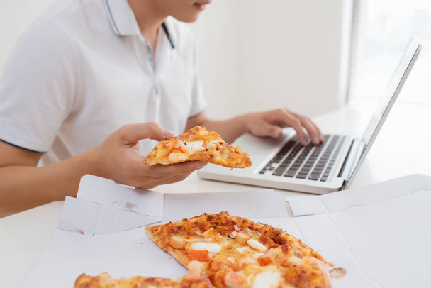 close up man hand eating pizza working in laptop computer - Fotó, kép
