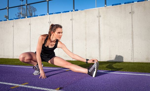 young athletic woman stretching on stadium running track before jogging  - Foto, afbeelding