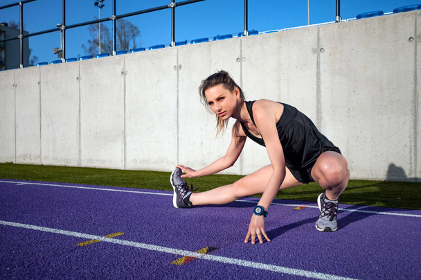 joven atlética mujer estirándose en pista de atletismo del estadio antes de correr
  - Foto, Imagen