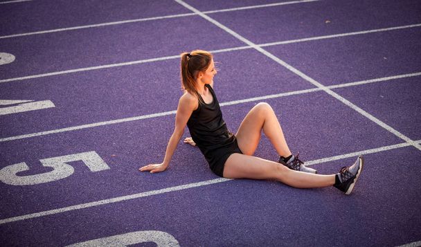 Young athletic woman resting  on studium track after training - 写真・画像