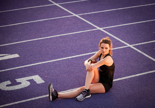 Young athletic woman resting  on studium track after training - Фото, изображение