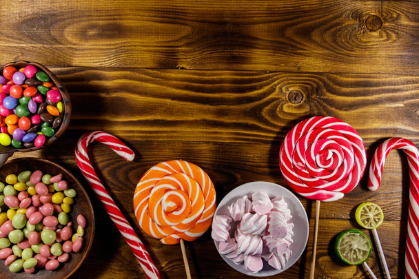 Kolorowe czekoladowe cukierki, lizaki, trzcina cukrowa i pianki na drewnianym stole - Zdjęcie, obraz