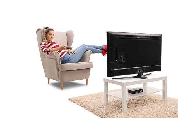 Молодая женщина, сидящая в кресле, смотрит телевизор и переключает каналы на белом фоне
 - Фото, изображение