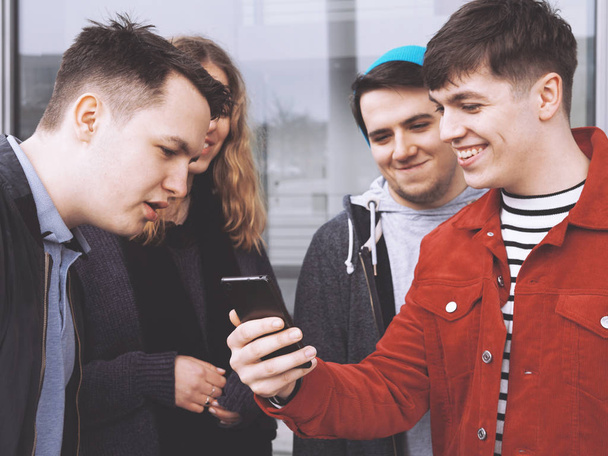 mladý muž ukazuje něco zábavného na jeho smartphone ke skupině dospívajících přátel - Fotografie, Obrázek