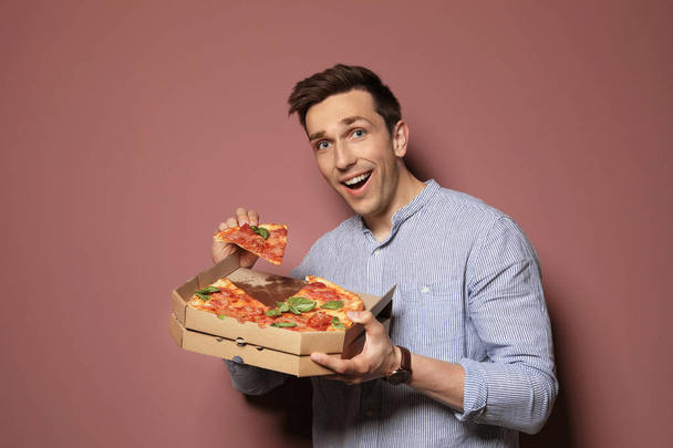 Aantrekkelijke jonge man met heerlijke pizza op kleur achtergrond - Foto, afbeelding