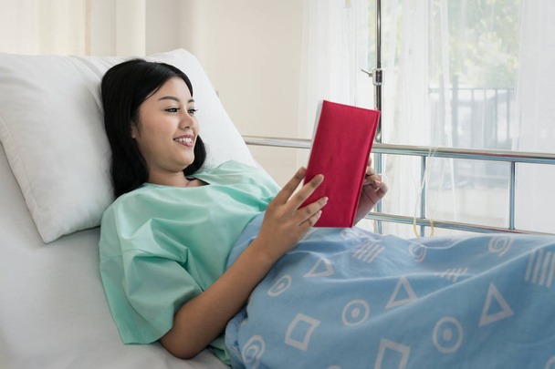 Ázsiai fiatal nő beteg olvasókönyv a kórházi ágyon fekve. Ő olvasott a pihenésre. - Fotó, kép