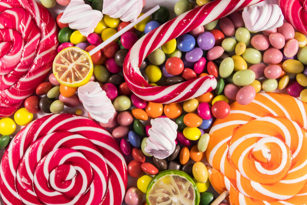Színes csokoládécukorkák, nyalókák, cukornád és mályvacukor háttere - Fotó, kép