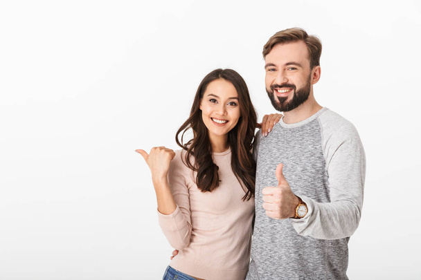 Image of cheerful young loving couple isolated over white wall background. Looking camera pointing make thumbs up. - Foto, Bild
