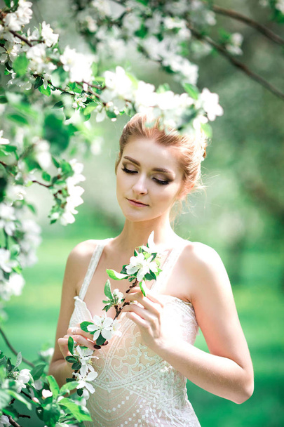Güzel kız elle çiçek açması bir elma ağacı dalı. Genç güzel sarışın bir kadın çiçek bahçesinde. Gelin. - Fotoğraf, Görsel