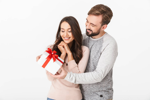 Image of happy young loving couple isolated over white wall background holding gift present box. - Zdjęcie, obraz