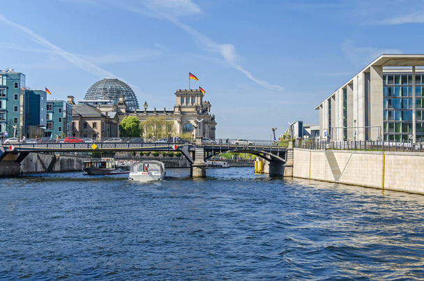 Berlín, Alemania - 22 de abril de 2018: Río Spree con barcos turísticos, el puente Marschallbruecke, el antiguo edificio del parlamento Reichstag y los nuevos edificios del parlamento Paul-Loebe House y Marie-Elisabeth-Lueders House a la derecha
 - Foto, imagen
