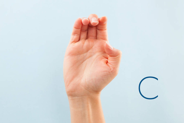 American sign language. Female hand showing letter C isolated on blue background.  - Photo, Image